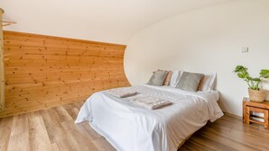 Ein Schlafzimmer mit gewölbter Decke, einer Holzwand und einem Bett mit weißer Bettwäsche. Ein kleiner Nachttisch aus Holz beherbergt eine Pflanze.