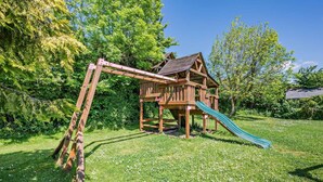Ein hölzernes Spielhaus mit Rutsche und einer Leiter in einem grünen Garten.