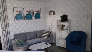 A modern room with a grey sofa, a blue armchair, a white bookshelf, and abstract wall art. - 4. Moderno Departamento Entero Estilo Minimalista - CUARTO PISO (Breña)