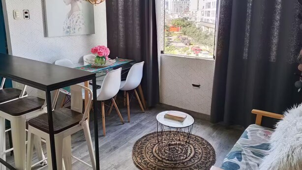 A modern apartment with a dining area, a round coffee table, a sofa, and a view of buildings through a large window. - 4. Moderno Departamento Entero Estilo Minimalista - CUARTO PISO (Breña)