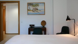 A hotel room with a bed, desk, chair, lamp, and a painting of a beach scene. - Cosy apartment for 4 guests with WIFI, hot tub, TV and patio (Acquarossa)