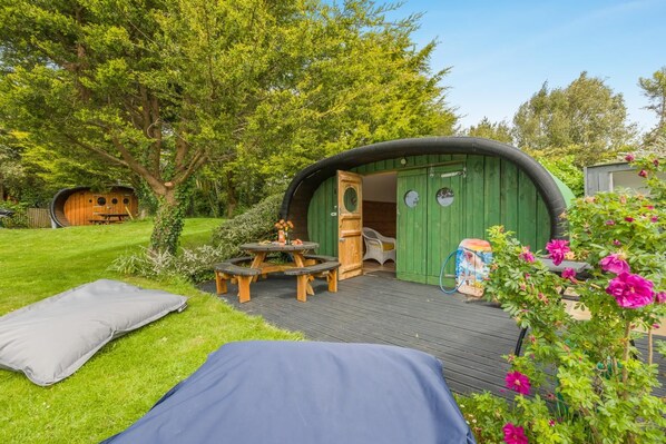 Een gezellig buitengebied met een houten terras, een picknicktafel en een groen bouwwerk met een gebogen dak.