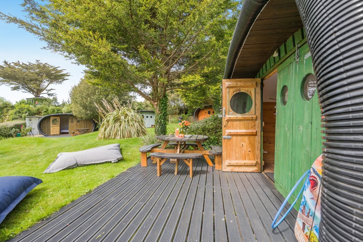 Eine Holzterrasse mit Picknicktisch und Bänken, umgeben von Grünflächen und einem kleinen Garten.