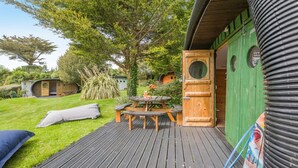 Eine Holzterrasse mit Picknicktisch und Bänken, umgeben von Grünflächen und einem kleinen Garten.