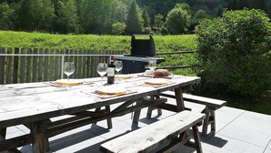 Ein Picknicktisch mit Weingläsern, einer Flasche und Brot, vor der Kulisse eines üppigen, grünen Feldes und bewaldeter Hügel.