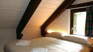 Ein Schlafzimmer mit schräg gedachter Decke, einem Bett mit weißer Bettwäsche und einem Fenster mit Vorhängen.