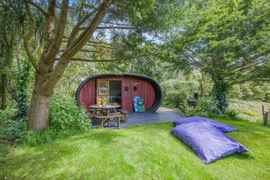 A rustic wooden structure with a circular entrance, a picnic table, and a sleeping area with a bed.