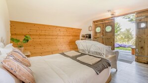 A bedroom with a wooden headboard, a bed with white bedding, a white wicker chair, and a view of the outdoors through a glass door.