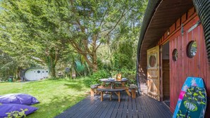 A wooden deck with a picnic table, a covered grill, and a small shed in a lush garden.