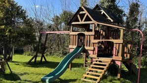 A wooden playhouse with a slide and stairs.