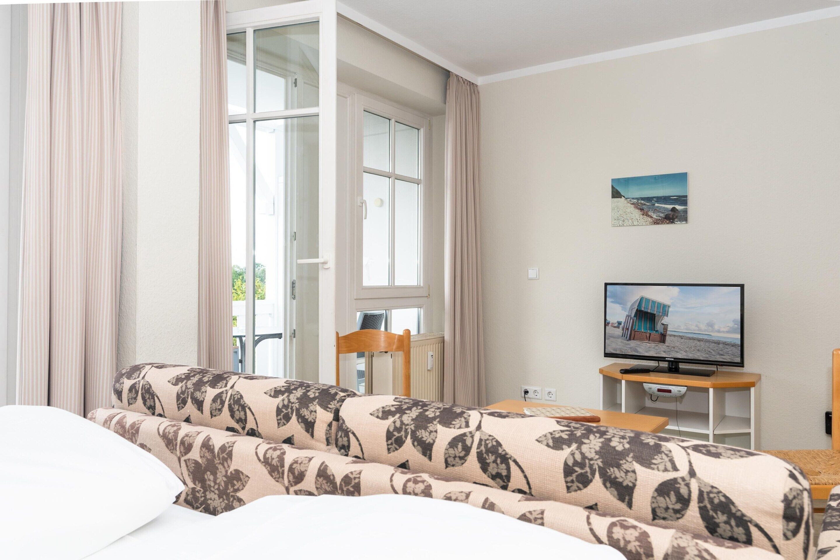 Una habitación con sofá, televisor sobre un mueble, una silla y una ventana con cortinas.
