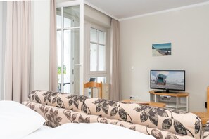 A room with a sofa, a television on a stand, a chair, and a window with curtains. - Ferienwohnung mit Moblierten Balkon in Sellin (Sellin)