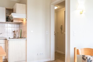 A kitchen with cabinets, a countertop, and a sink. There is a chair with a floral cushion and a wall-mounted light fixture. - Ferienwohnung mit Moblierten Balkon in Sellin (Sellin)