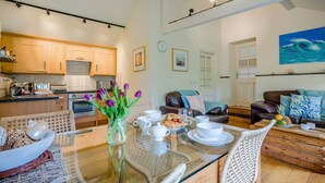 Uma cozinha moderna com armários de madeira, uma sala de jantar com uma mesa de vidro e uma sala de estar com um sofá e um quadro.