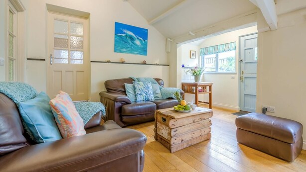 Uma sala de estar com um sofá de couro marrom, uma mesa de centro de madeira com frutas e um quadro azul na parede.