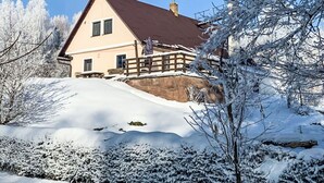 A two-story house with a brown roof, a stone foundation, and a wooden deck.