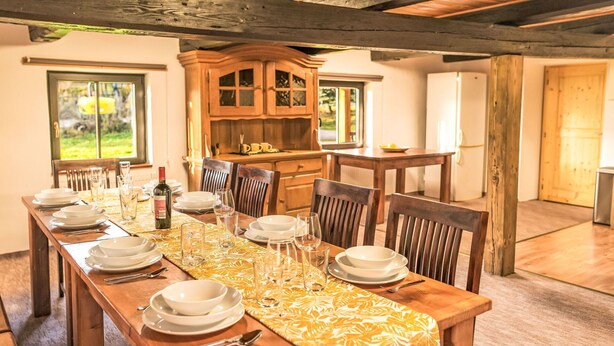 A dining room with a long wooden table set for a meal, wooden chairs, a cabinet, and a window with a view.