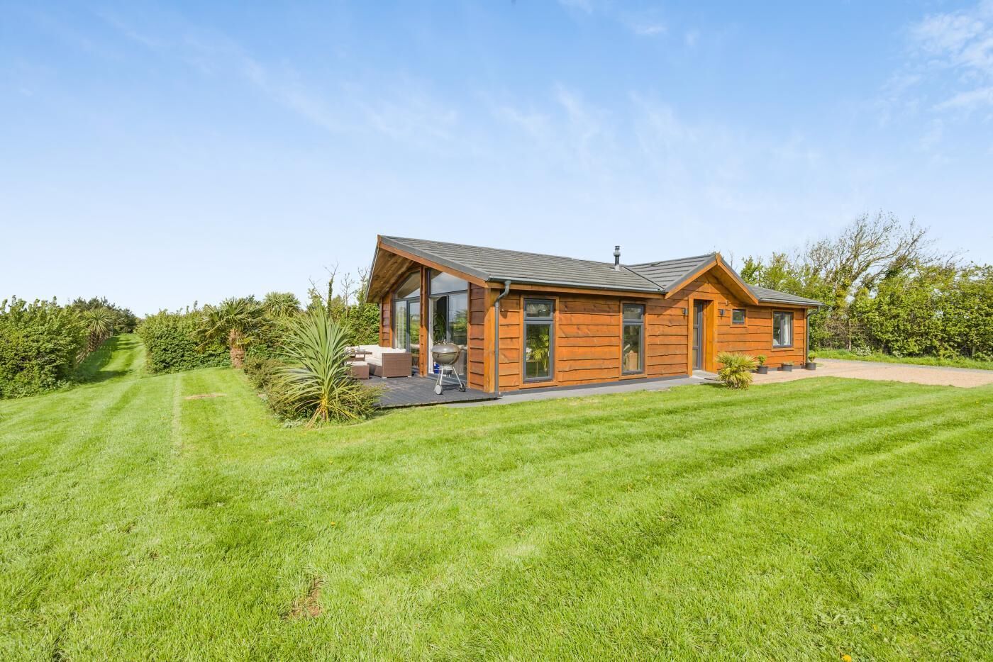 Ein modernes Blockhaus mit Terrasse, Grill und gepflegtem Rasen.