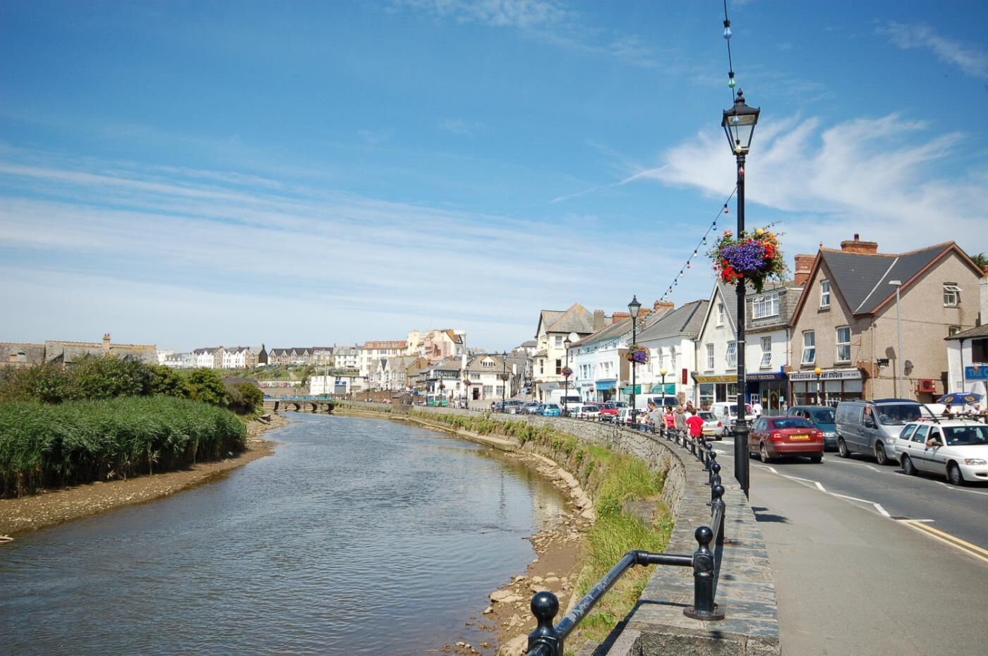 A riverside town with a paved walkway, buildings, and a bridge.