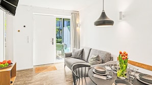Ein moderner Essbereich mit einem für zwei Personen gedecktem Tisch, einem grauen Sofa und Blick durch eine Glastür auf einen Außenbereich.