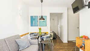 Ein modernes Wohnzimmer mit einer Couch, Esstisch und Stühlen, einem flachbildfernseher an der Wand und einem kleinen Holztisch mit Obst.