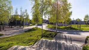 Ein Park mit einer Beton-Skateanlage, Bänken und Bäumen.