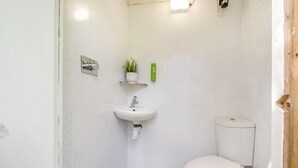 Ein kleines, weißes Badezimmer mit Waschbecken, Toilette und Ablagefläche mit einem Blumentopf.