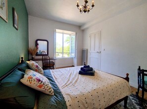 A bedroom with a bed, a chair, a dresser, a mirror, and a window.