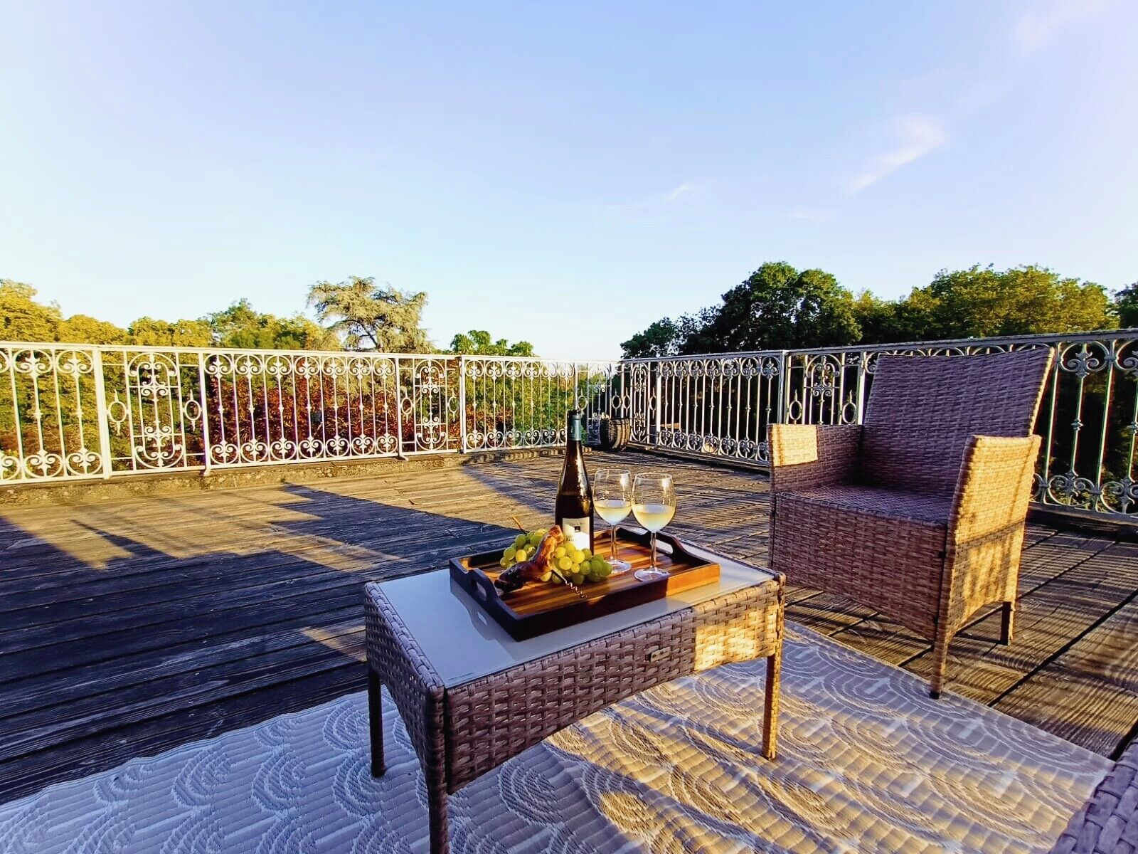 Een terras op het dak met een rieten tafel, twee stoelen en een fles wijn.