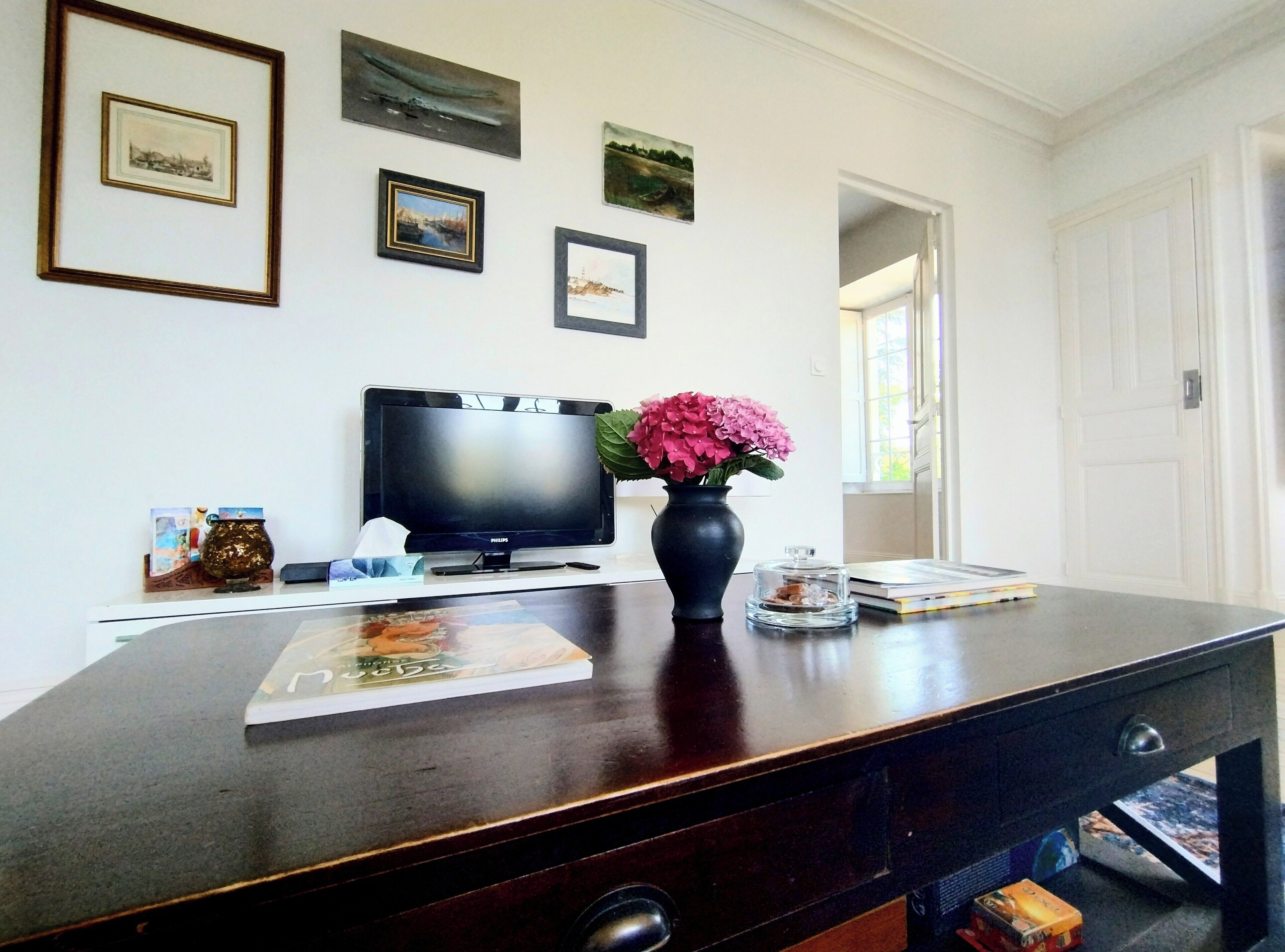 Een kamer met een flatscreen televisie, een vaas met bloemen en lijstwerken aan de muur.