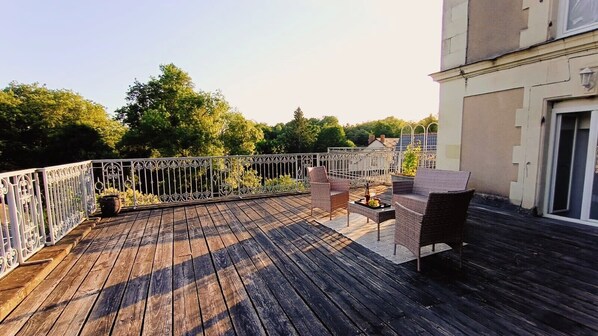A wooden deck with outdoor furniture, a metal railing, and a building in the background.