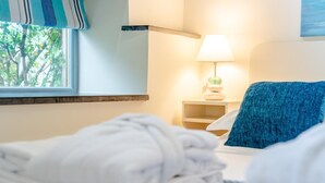 Ein Hotelzimmer mit einem Bett, einem Nachttisch mit Lampe, einem Fenster mit Blick auf Bäume und einem blauen Handtuch auf dem Bett.