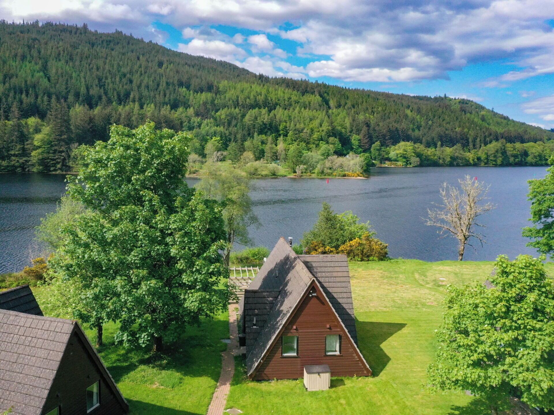 A cabin with a sloped roof, surrounded by lush greenery and a lake.