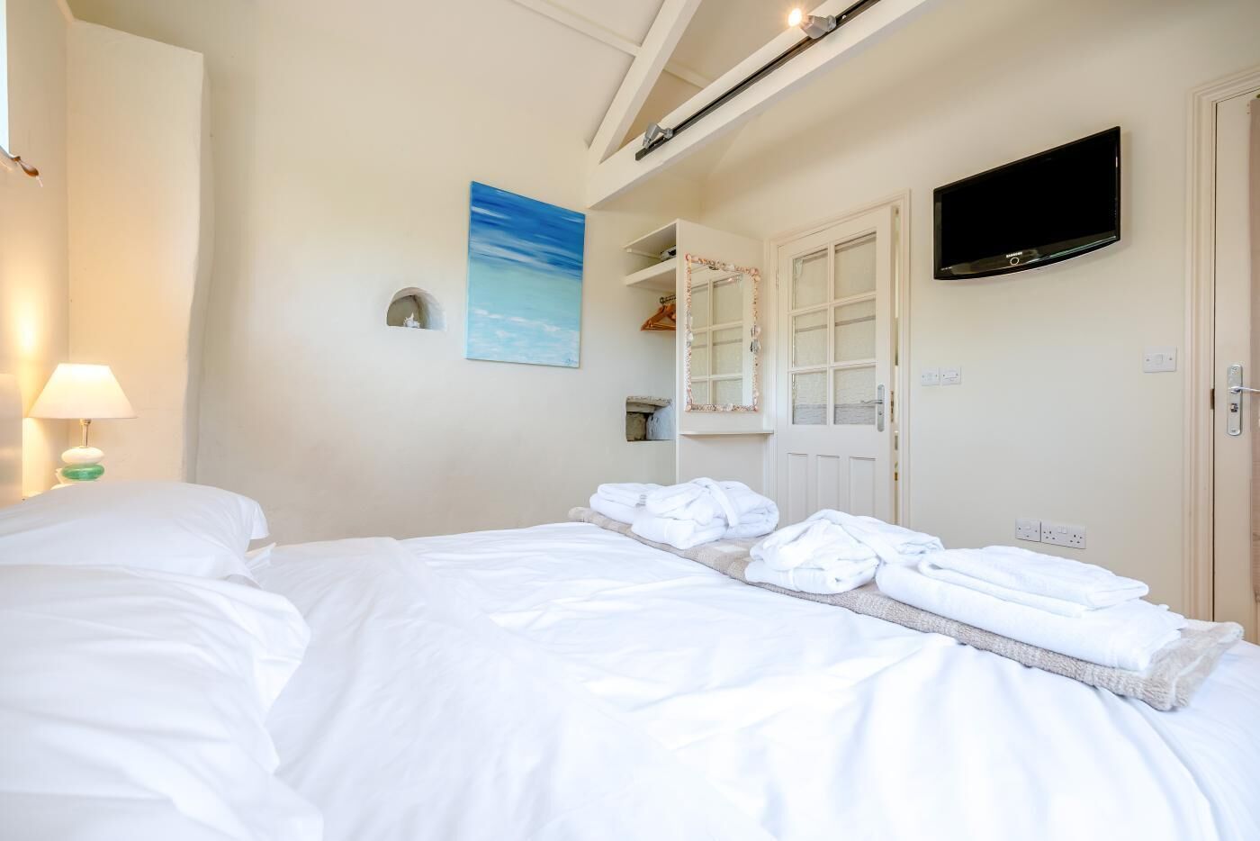 Une chambre d’hôtel avec un lit, un téléviseur à écran plat, un tableau et un miroir.