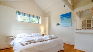 A bedroom with a bed, a nightstand, a window with blinds, a wall-mounted mirror, and a painting. - 2 Bed in Bude (oc-c34841) (Bude)