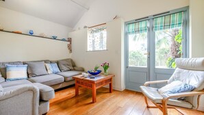 A living room with a sofa, a wooden coffee table, a chair, and a door with a window. - 2 Bed in Bude (oc-c34841) (Bude)