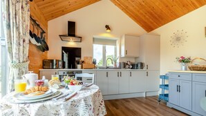A kitchen with wooden ceiling, white cabinets, and a dining table set with breakfast.