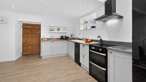 A modern kitchen with grey cabinets, a wooden door, a black range hood, and a built-in oven. - 1 Bed in Bontuchel (oc-t34921) (Bontuchel)