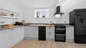 A modern kitchen with white cabinets, a black dishwasher, a stove, and a refrigerator. - 1 Bed in Bontuchel (oc-t34921) (Bontuchel)