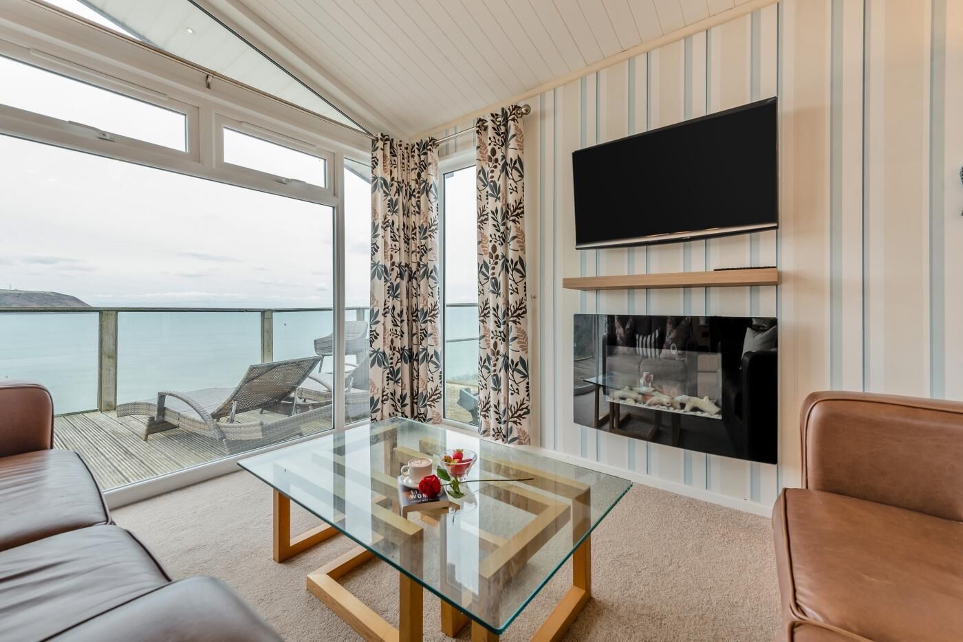 Ein modernes Wohnzimmer mit Glastisch, Ledersofas, Flachbildfernseher und Kamin.