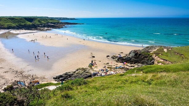 Une plage animée, un rivage rocheux et des collines verdoyantes.