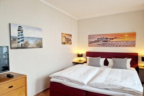 A hotel room with a bed, two bedside tables, a TV, and wall art depicting coastal scenes. - Komfortable Ferienwohnung im Seepark Sellin mit Balkon (Sellin)