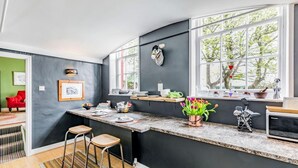 Une cuisine dotée d’un comptoir incurvé, de tabourets de bar, d’une fenêtre offrant une vue agréable et d’une chaise rouge dans la pièce adjacente.