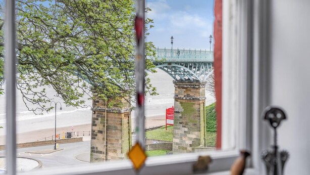 Une vue à travers une fenêtre d’une structure en pierre, d’un pont métallique et d’un panneau rouge.