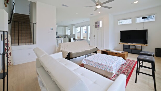 A modern living room with a sofa, a TV, a ceiling fan, and a staircase leading to a kitchen. - New Townhouse near DFW FIFA ATT STADIUM (North Richland Hills)