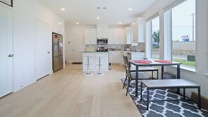 A modern kitchen with white cabinets, a stainless steel refrigerator, a microwave, and a dining area with a table and chairs. - New Townhouse near DFW FIFA ATT STADIUM (North Richland Hills)