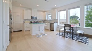 A modern kitchen with white cabinets, a central island with stools, a microwave, and a dishwasher. - New Townhouse near DFW FIFA ATT STADIUM (North Richland Hills)