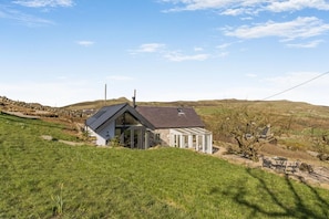 Une maison avec un toit en pente, une véranda en verre et un mur de pierre, située dans un cadre rural.