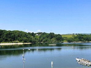 Ein ruhiger See mit Booten, einer Anlegestelle und einem bewaldeten Hügel.
