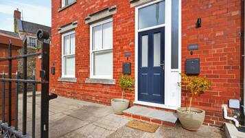 A red brick house with a blue door, two windows, a gated entrance, and two potted plants.